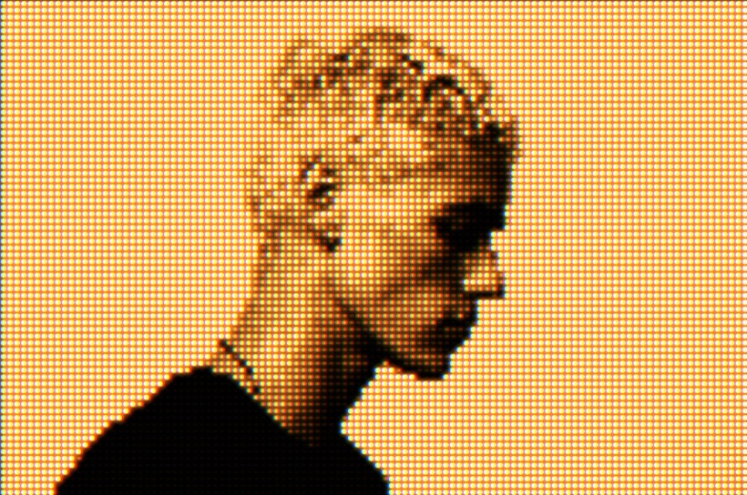 A portrait rendered as a glowing amber LED dot-matrix display, like an LED sign or scoreboard